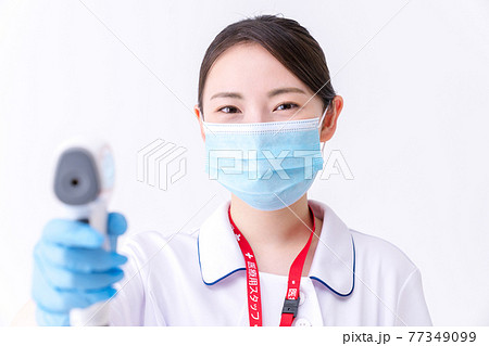 非接触体温計で体温測定をする看護師 非接触体温計で体温測定をする看護師 77349099