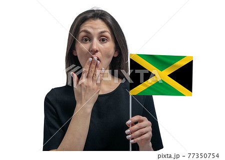 Happy young white woman holding flag of Jamaica and covers her mouth with her hand isolated on a white background 77350754