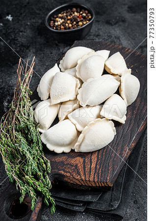 Frozen raw dumplings pierogi with potato on a wooden board. Black background. Top View Frozen raw dumplings pierogi with potato on a wooden board. Black background. Top View 77350793