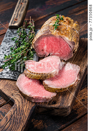 Roast Tenderloin beef fillet meat on a wooden board with herbs. Dark wooden background. Top view 77350868