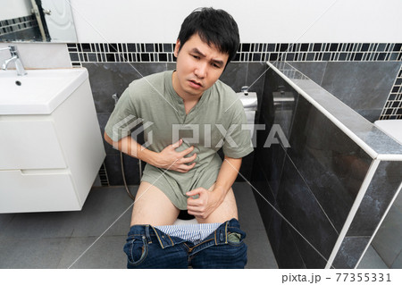 unhappy man with stomach issues sitting in toilet bowl in bathroom 77355331