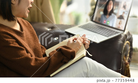 Beautiful woman taking notes while sitting in front her laptop at the leather couch in living room. Work from home/Remote working concept. Working from home through video conference concept. Beautiful woman taking notes while sitting in front her laptop at the leather couch in living room. Work from home/Remote working concept. Working from home through video conference concept. 77359448