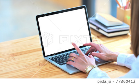 Cropped image of creative woman's hands typing on computer laptop that putting on wooden working desk and surrounded by stack of books, pencil holder, coffee cup and potted plant. Orderly workspace. Cropped image of creative woman's hands typing on computer laptop that putting on wooden working desk and surrounded by stack of books, pencil holder, coffee cup and potted plant. Orderly workspace. 77360412