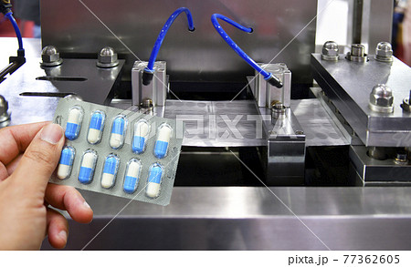 Hand holding blue capsule pack at medicine pill production line, Industrial pharmaceutical concept. 77362605