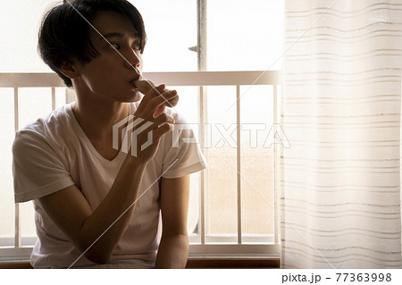 暑い日に部屋でアイスを食べる男性 77363998