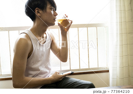 部屋で飲み物を飲む男性 77364210