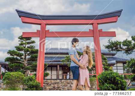 Happy couple travelers in medical mask looking at the Japanese traditional building. Tourists travel in Japan after the coronavirus epidemic Happy couple travelers in medical mask looking at the Japanese traditional building. Tourists travel in Japan after the coronavirus epidemic 77366257