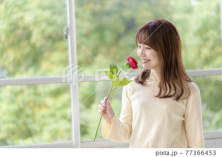 笑顔で薔薇の匂いを嗅ぐ若い女性 77366453