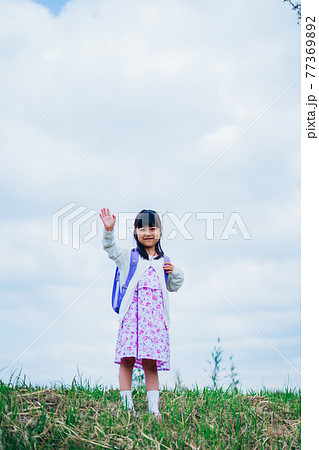 ランドセルを背負って手を振る小さな女の子 77369892