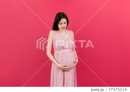 a pregnant girl who has a stomach ache stands on a colored background. isolated a pregnant girl who has a stomach ache stands on a colored background. isolated 77373214