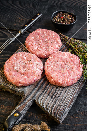 Raw chicken turkey patty, ground meat cutlets on a chopping Board. Black wooden background. Top view 77376346