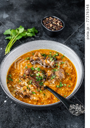 Lamb soup Kharcho with mutton meat, rice, tomatoes and spices in a bowl. Black background. Top view 77376348