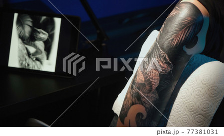 Close up photo of man doing tattoo of snake for woman in studio Close up photo of man doing tattoo of snake for woman in studio 77381031