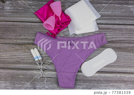 Women's panties with menstrual cups, sanitary pads and tampons on wooden background. Top view. Concept of critical days, menstruation, feminine hygiene 77381339