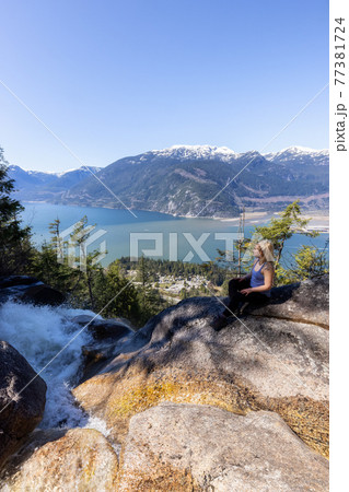 Adventurous Adult Woman is sitting on top of a Beautiful Waterfall Adventurous Adult Woman is sitting on top of a Beautiful Waterfall 77381724