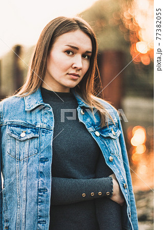 Portrait of the attractive, slender, beautiful young Caucasian blonde girl in a jeans jacket. Smiling girl enjoys fine warm sunner weather against the forest 77382055