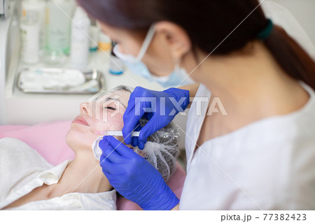 Beautiful woman at the dermatology clinic. Cosmetologist doing injections on the face and mouth area of female client. Skin biorevitalizing and anti-aging therapy. Beautiful woman at the dermatology clinic. Cosmetologist doing injections on the face and mouth area of female client. Skin biorevitalizing and anti-aging therapy. 77382423