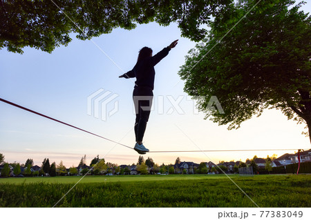 Adventurous White Caucasian Adult Woman walking on a Slackline Adventurous White Caucasian Adult Woman walking on a Slackline 77383049