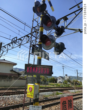 青空の下で踏切が危険を知らせる。ある晴れた日の出来事。 77384824