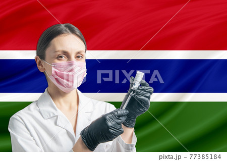 Girl doctor prepares vaccination against the background of the Gambia flag. Vaccination concept Gambia 77385184