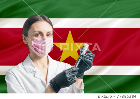 Girl doctor prepares vaccination against the background of the Suriname flag. Vaccination concept Suriname 77385284