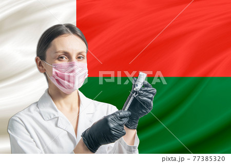 Girl doctor prepares vaccination against the background of the Madagascar flag. Vaccination concept Madagascar 77385320