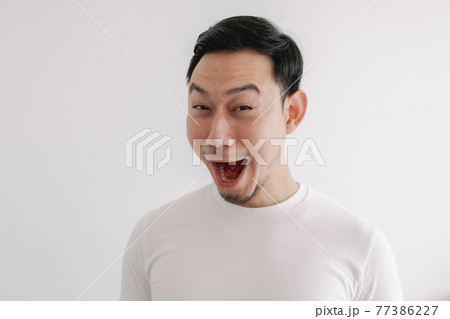 Funny grin smile face of man in white t-shirt isolated on white wall. 77386227