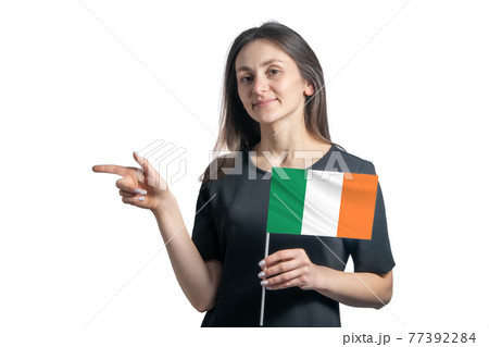 Happy young white woman holding flag Ireland and points to the left isolated on a white background 77392284