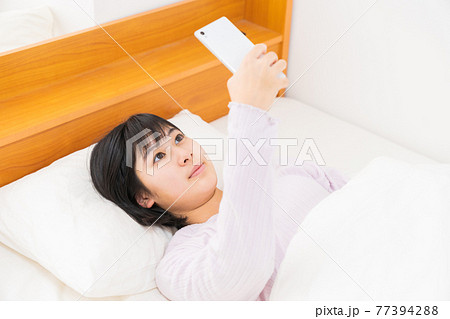 ベッドでスマホを見る女の子 77394288