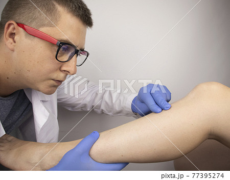 The podiatrist examines the tibia of a patient who complains of pain in it. The concept of diagnostics of bone microcracks and latent course of diseases The podiatrist examines the tibia of a patient who complains of pain in it. The concept of diagnostics of bone microcracks and latent course of diseases 77395274