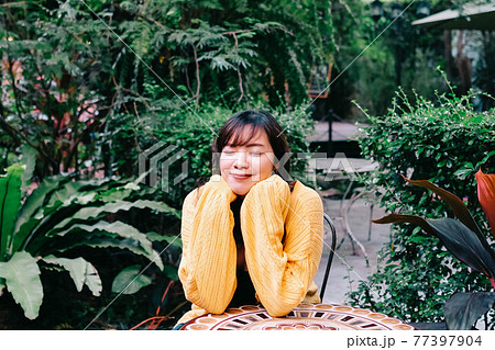 Close up of young pretty Asian woman in blue yellow sweater with garden background. 77397904