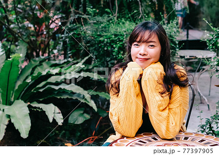 Close up of young pretty Asian woman in blue yellow sweater with garden background. 77397905