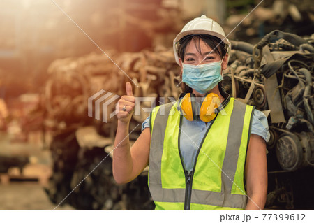 Asian women worker thumbs up waring face mask happy working safety work in a heavy industrial factory with engine machine background 77399612
