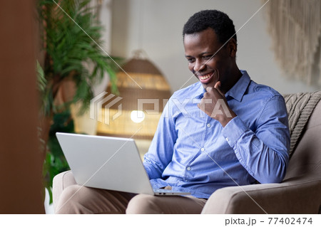 Young positive smiling african man typing on laptop at home Young positive smiling african man typing on laptop at home 77402474