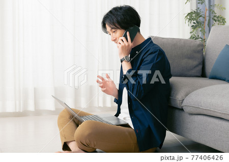 床に座ってテレワークする若い男性 床に座ってテレワークする若い男性 77406426