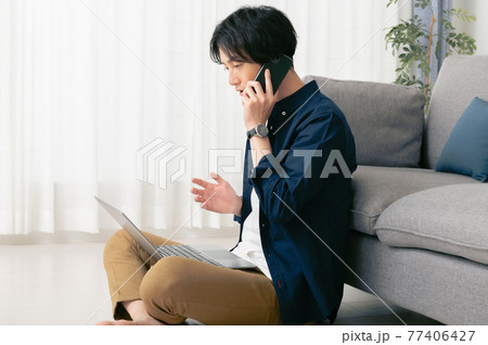 床に座ってテレワークする若い男性 77406427