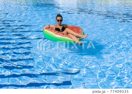 Summer fun. Happy young sexy girl in bikini swimsuit, sunglasses with inflatable rubber ring floating in blue pool water. Having fun and enjoying travel vacation. Swimming pool water. 77409335