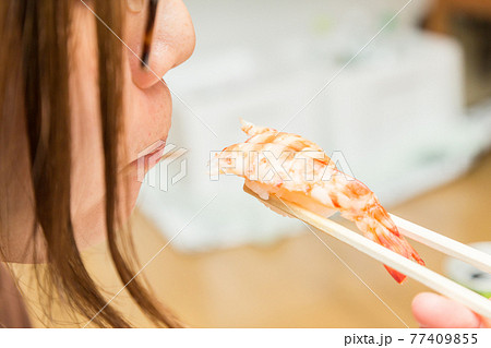 エビの握りずしを食べる女性の手元 77409855