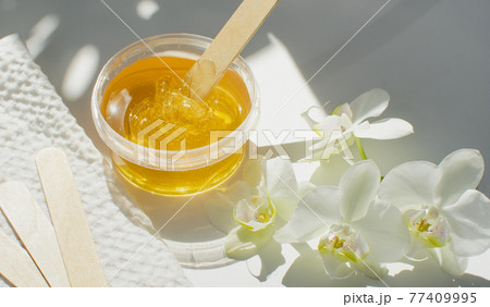Sugar paste or wax honey in a transparent jar on a white background. Sugaring. Depilation and beauty concept. Waxing. Sugar paste or wax honey in a transparent jar on a white background. Sugaring. Depilation and beauty concept. Waxing. 77409995