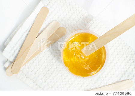 Sugar paste or wax honey in a transparent jar on a white background. Sugaring. Depilation and beauty concept. Waxing. 77409996