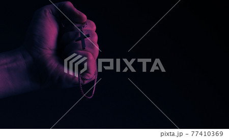 Praying with a rosary. hand of Catholic man with rosary on black background. Hands holding a silver rosary or cross pendant of Jesus Christ. Crucifix and hand on black background. Praying God concept Praying with a rosary. hand of Catholic man with rosary on black background. Hands holding a silver rosary or cross pendant of Jesus Christ. Crucifix and hand on black background. Praying God concept 77410369