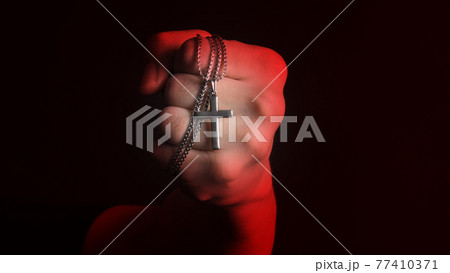 Praying with a rosary. hand of Catholic man with rosary on black background. Hands holding a silver rosary or cross pendant of Jesus Christ. Crucifix and hand on black background. Praying God concept Praying with a rosary. hand of Catholic man with rosary on black background. Hands holding a silver rosary or cross pendant of Jesus Christ. Crucifix and hand on black background. Praying God concept 77410371