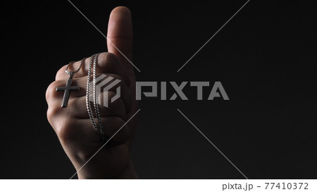 Praying with a rosary. hand of Catholic man with rosary on black background. Hands holding a silver rosary or cross pendant of Jesus Christ. Crucifix and hand on black background. Praying God concept Praying with a rosary. hand of Catholic man with rosary on black background. Hands holding a silver rosary or cross pendant of Jesus Christ. Crucifix and hand on black background. Praying God concept 77410372