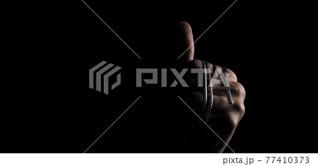 Praying with a rosary. hand of Catholic man with rosary on black background. Hands holding a silver rosary or cross pendant of Jesus Christ. Crucifix and hand on black background. Praying God concept 77410373