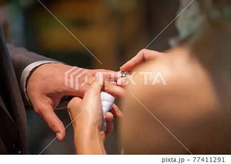 Closeup of bride putting a wedding ring onto the groom's finger. Couple exchanging wedding rings. 77411291