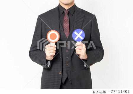 白背景の前に立って、OKとNGのプラカードを持っている男性ビジネスマン 77411405