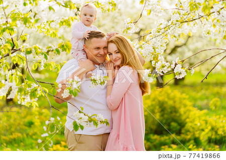 family with a baby daughter in spring flowering garden. cleft lip in infants. 77419866