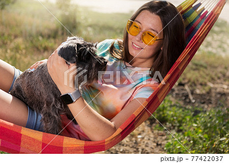 girl lying in a hammock in sunglasses holding a miniature schnauzer in her arms, lifestyle concept 77422037