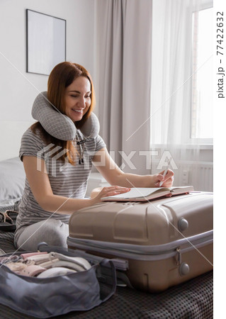 Smiling tourist woman packing suitcase to vacation writing paper list getting ready to travel trip 77422632