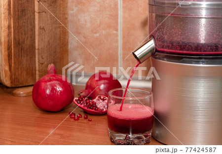 Pomegranate juice pours from a juicer into a glass. Making juice at home. 77424587